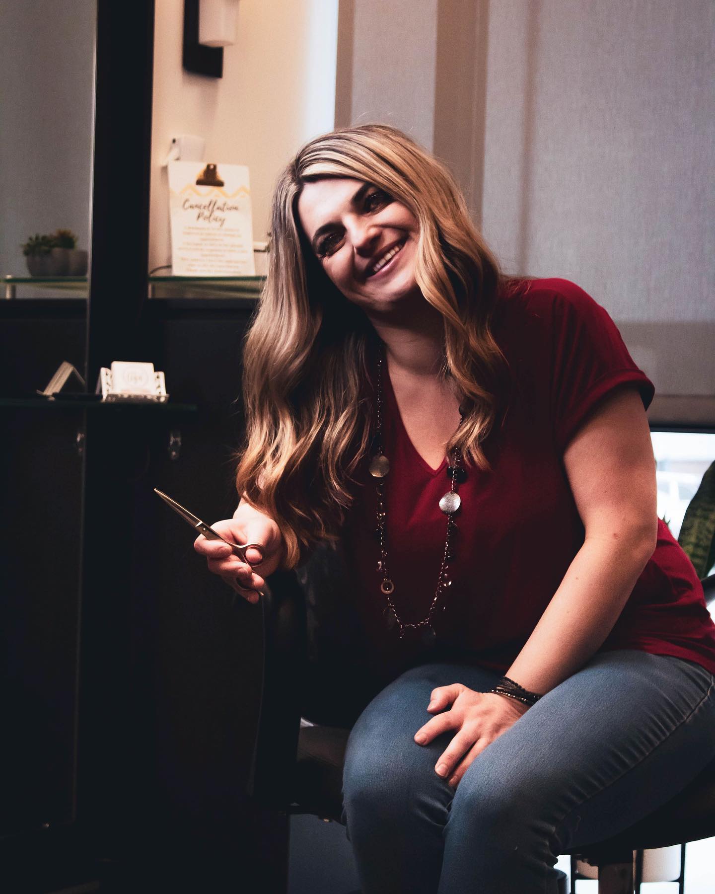 Stylist smiling in a salon while holding haircutting shears.